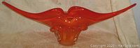 Side view of long orange glass vase with pointed ends and abstract lips shape.
