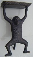 Front angle of bronzed metal monkey card holder figure with arms raised holding flat textured platform.