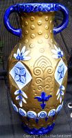 Close-up photo of Amphora pottery vase showing blue floral and geometric embossed motifs and handles