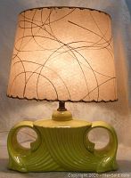 Front view of the lamp lit, showing ceramic base and parchment shade with black and gold abstract lines.