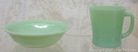 Side view of the pale green Fire King Jadeite bowl and matching coffee mug on a fabric background.