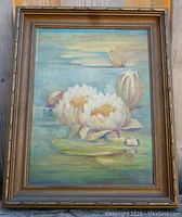 Full view of oil painting in ornate wood frame depicting white water lilies floating on water with blue sky background.