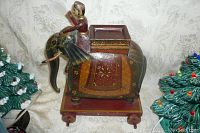 Front angle view of carved wooden elephant pull-toy with seated figure and decorative painted covering on wheeled wooden base.