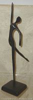 Front view of abstract bronze ballerina statue with raised leg and arm, standing on square base.