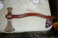 Full view of the tomahawk showing wooden handle and brass head laying on table.