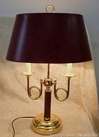 Front view of brass desk lamp with burgundy shade, showing base, arms, and shade detail.