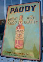 Front view of the tin sign showing the Paddy whiskey bottle and advertising text under glazing or reflection.