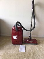 Full view of vacuum canister with hose, wand, floor head and manual laid out