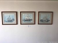Photo showing all three framed 1984 tall ship prints hanging on a wall with city skylines in the background.