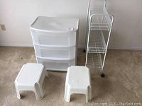 Photo showing plastic 3-drawer container, two small white plastic step stools, and metal wire rack.