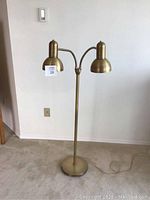 Front view of the brass floor lamp showing two dome-shaped adjustable lampshades and round base on carpet.