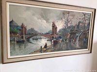 Framed oil painting showing a Paris cityscape with a prominent bridge over water, pedestrians on the right, and boats on the left. The sky is cloudy and the overall tone is moody.