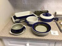 Blue and white ceramic bakeware and serving dishes arranged on counter showing variety of shapes and sizes including rectangular baking dishes, plates, small pitcher, and lidded casserole dish.