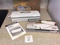 Closed view of Toastess electronic vacuum bag sealer, instruction booklet, and polyethylene roll refill pack box on countertop.