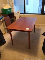 Rectangular table in room, showing teak-like finish and tapered legs.