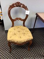 Full view of vintage carved wooden chair with tufted cushioned seat on patterned carpet