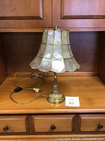 Front view of vintage brass base table lamp with brass-outlined lampshade on wooden surface.
