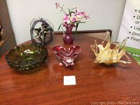 Photo of four glass centerpieces on a wooden table, showing green bowl, cranberry vase, amber centerpiece, and hanging glass item.