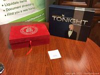 Red box with President of the United States seal and The West Wing title with adjacent black box of The Tonight Show on wooden table.