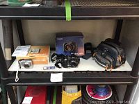 Two Canon digital cameras, their boxes, memory cards, and carrying case arranged on a shelf