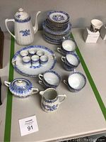 Porcelain tea and serving set laid out on table showing cups, plates, cream pitcher, sugar bowl, and coffee pot with blue floral patterns