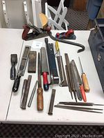 Photo of assorted hand tools laid out on table showing two hand planes, files, chisels, crowbar, sharpening stones, and saw blades.