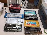 Photo showing all items together: Century battery charger, one blue tap and die set, and four ratchet socket sets in metal cases.