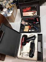 Two Weller solder guns with accessories inside two molded black plastic carrying cases on a table.