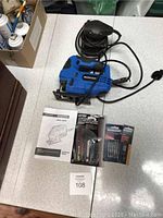 Photo showing Mastercraft orbital jigsaw, palm sander, instruction manual, and packs of jigsaw blades on a tabletop.