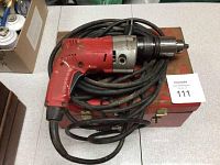 Red Milwaukee Magnum Hammer Drill with attached power cord coiled and resting on top of red metal carrying case.