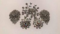 Rhinestone brooch and earring sets arranged grouped on a white background showing clear and multi-colored rhinestones.