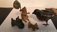 Photo showing four figurines on a flat surface: lead pig, bronze bird, carved clay dog, and small carved clay bird.
