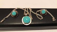 Front view of necklace with turquoise pendant and matching stud earrings on black background.