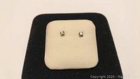 Diamond stud earrings on cream cushion, shown on black background