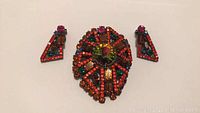 Front view of vintage multi-colored rhinestone brooch and matching triangular earrings on white background.