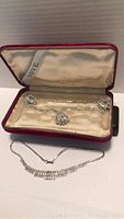 Necklace and earrings displayed inside red velvet Dove box with satin lining, all pieces featuring clear rhinestones in silver setting.