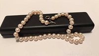 Pearl necklace stretched over a black case, showing white round pearls and toggle clasp