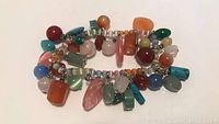 Top view of the multi-gemstone bracelet showing various polished beads and carved charms in multiple colors spread along the coil bracelet.