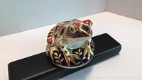 Front view of the hand-painted Royal Crown Derby frog figurine showing detailed gold accents and colorful patterns on a round base.
