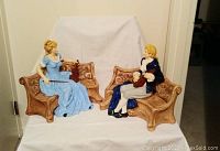 Photo showing both musician figurines seated on brown benches, depicting woman with violin and man with instrument.