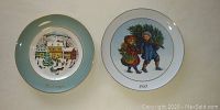 Two gold trimmed holiday plates, one from 1980 with a village winter snow scene, and one from 1981 with children carrying a Christmas tree.