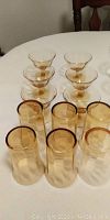 Photo of 12 amber glasses: 6 taller cylindrical drinking glasses and 6 smaller dessert glasses with stems, displayed on a table.