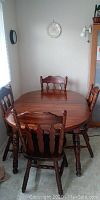 Angle view of oval honey pine dining table with six matching chairs surrounding it, showing wood grain and chair detail.