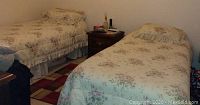 Two twin beds with framed mattresses covered in floral bedding; bedding not included in lot.