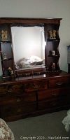 Wooden dresser with a large mirror featuring shelving and decorative accents. Mirror has a crack in the top left corner.