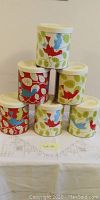 Photo of six vintage Crisco tins stacked in a pyramid, decorated with red and blue birds on green leafy background, each about 6 inches tall.