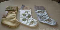 Full view of three satin Christmas stockings in gold, white, and silver with embroidery