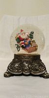 Christmas snow globe music box with Santa and elves on ornate metal base