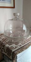 Glass cake dish with dome lid sitting on table with patterned cloth