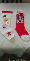 Two Christmas stockings laid flat on a table; one white with angel and red star, one red with knit Christmas tree.